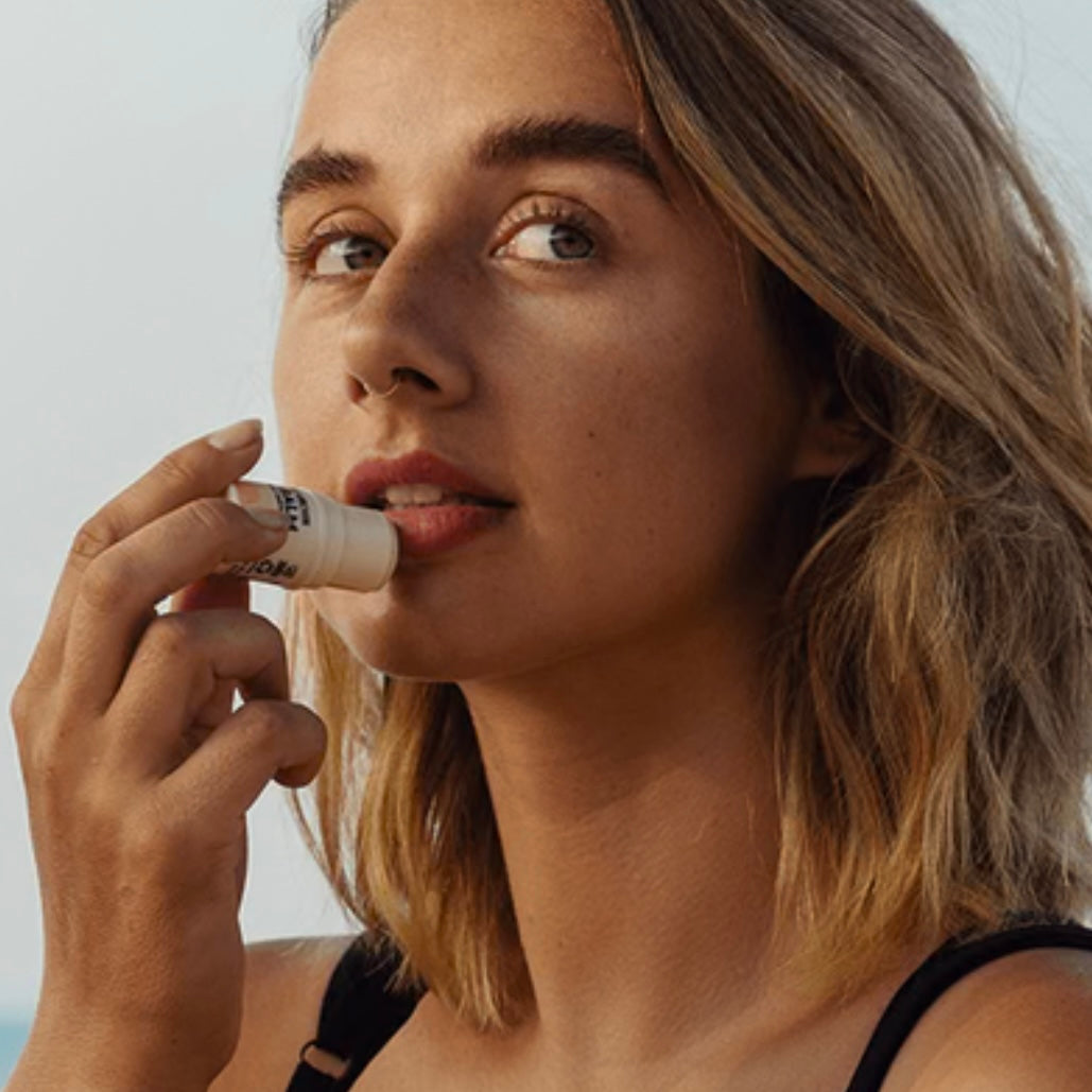 Woman applying lip balm with a LITTLE URCHIN background
