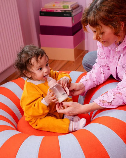Two children sitting on a striped bean bag, one holding a bottle.